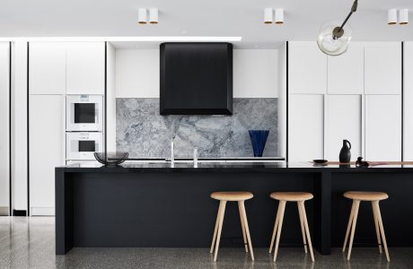 Modern kitchen with sleek black cabinetry, marble backsplash, and wooden bar stools.