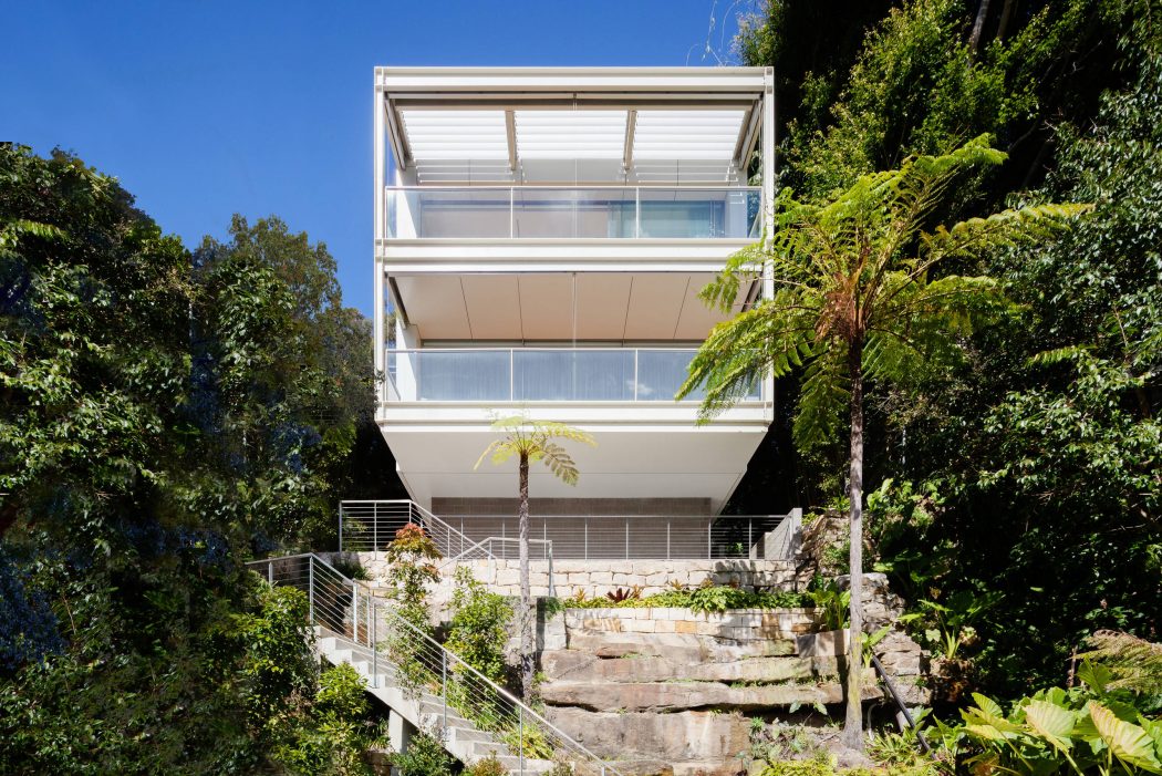 A modern, multi-story building with glass walls and balconies nestled among lush greenery.