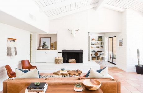 Bright, open-concept living room with white walls, wood beams, and a stone fireplace.