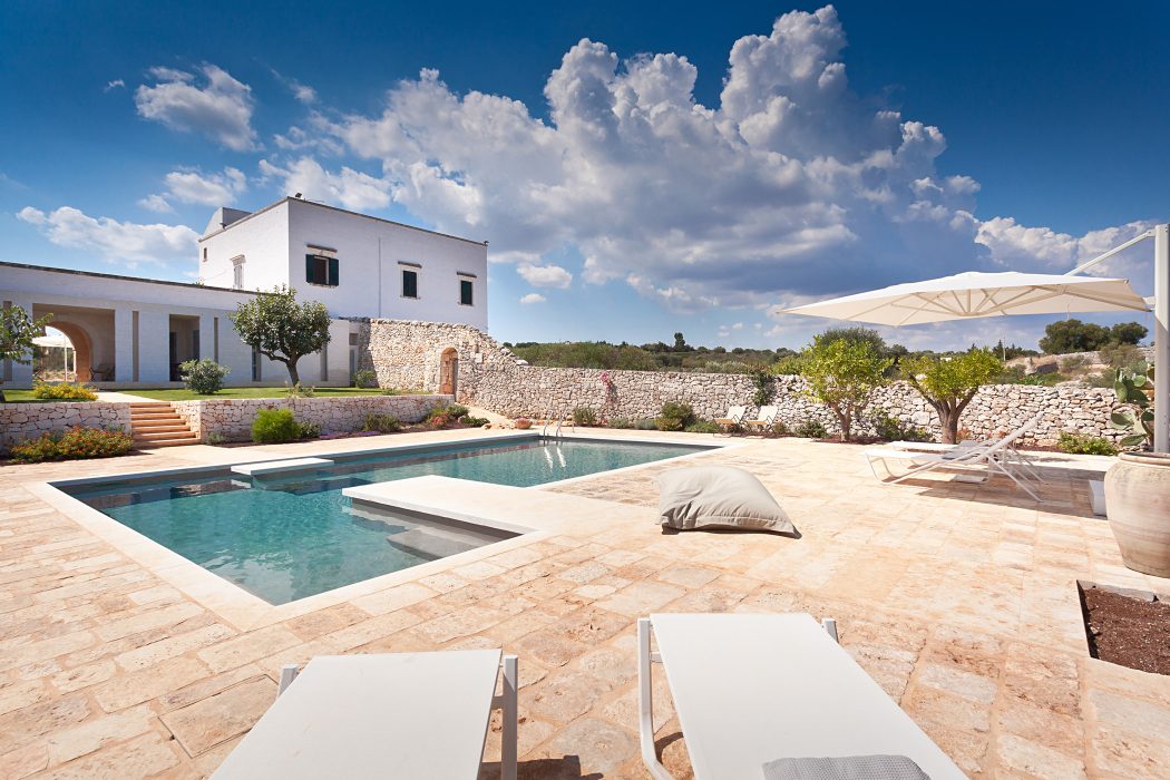 A picturesque Mediterranean villa with a stunning pool, stone walls, and lush landscaping.