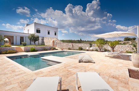 A picturesque Mediterranean villa with a stunning pool, stone walls, and lush landscaping.