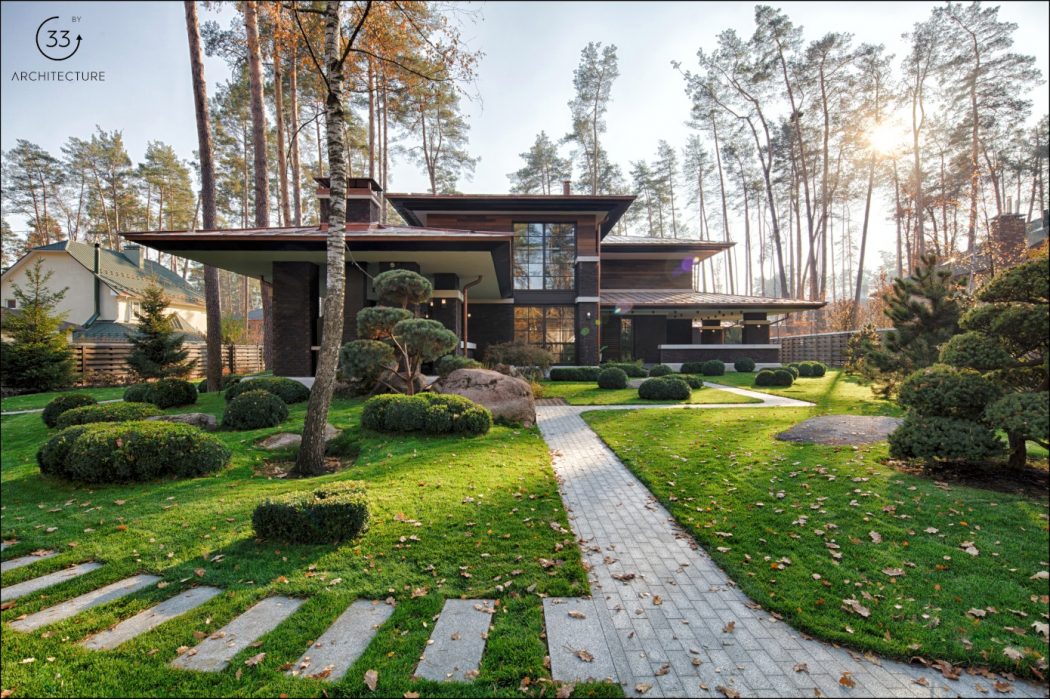 A modern, wooden house with a large glass facade, set in a lush, landscaped garden.