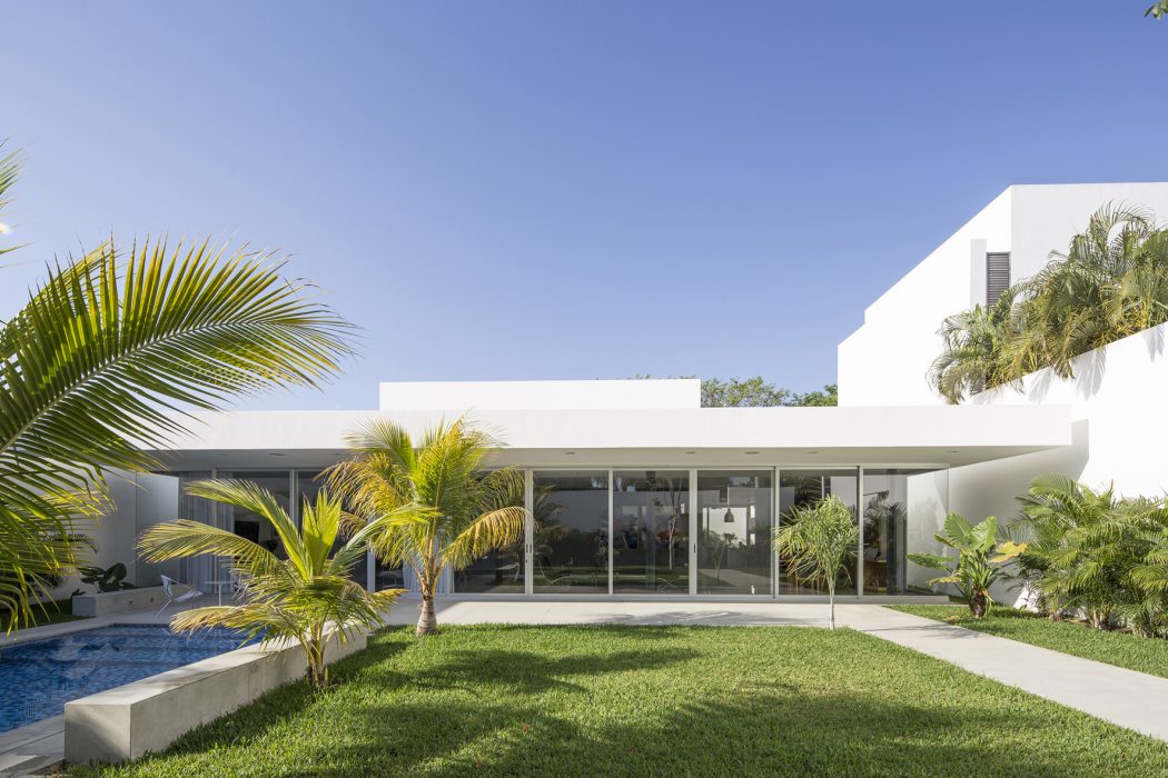 Sleek, modern architecture with glass walls, lush tropical landscaping, and a swimming pool.