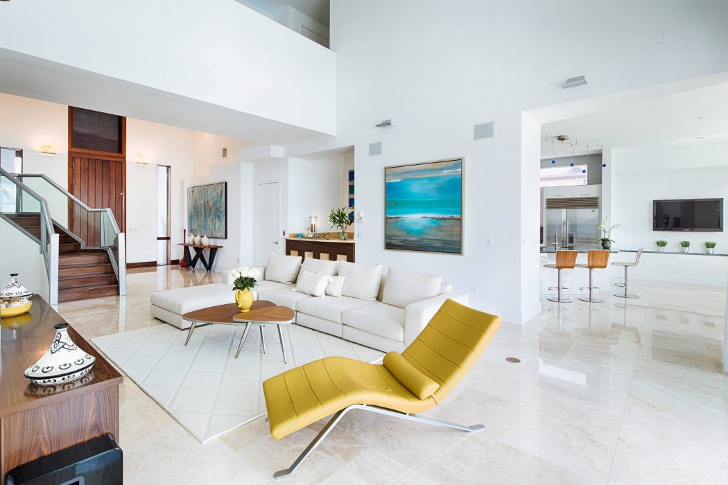 Spacious, modern living area with sleek white furniture, vibrant yellow chair, and coastal artwork.