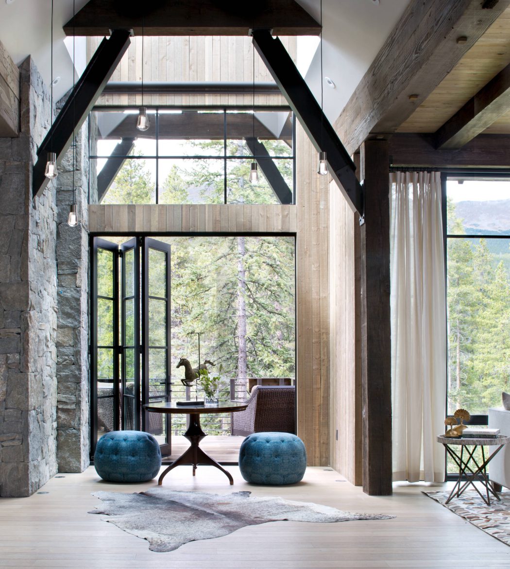 Rustic yet modern interior with wooden beams, large windows, and plush teal ottomans.