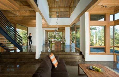 A modern, open-concept home with expansive windows, wood-lined ceilings, and sleek stairs.