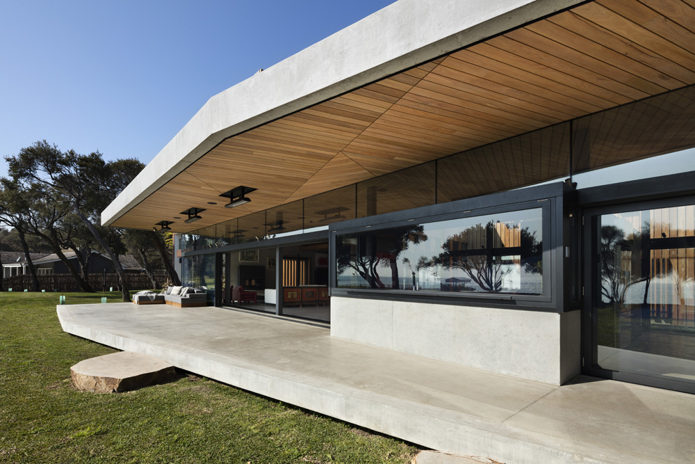 Modern glass-walled structure with a curved, wooden-paneled ceiling and stone foundation.