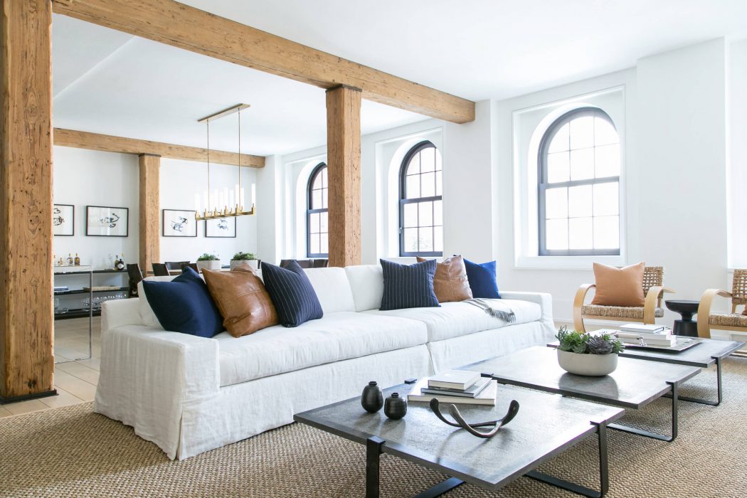 Bright, modern living room with exposed wooden beams, arched windows, and cozy furnishings.