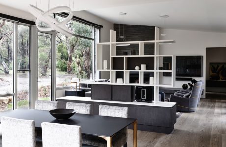 Modern open-concept living space with sleek furniture, shelving, and large windows overlooking nature.