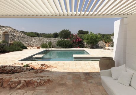 Rustic stone walls, sleek pool, and lush greenery create a serene Mediterranean oasis.