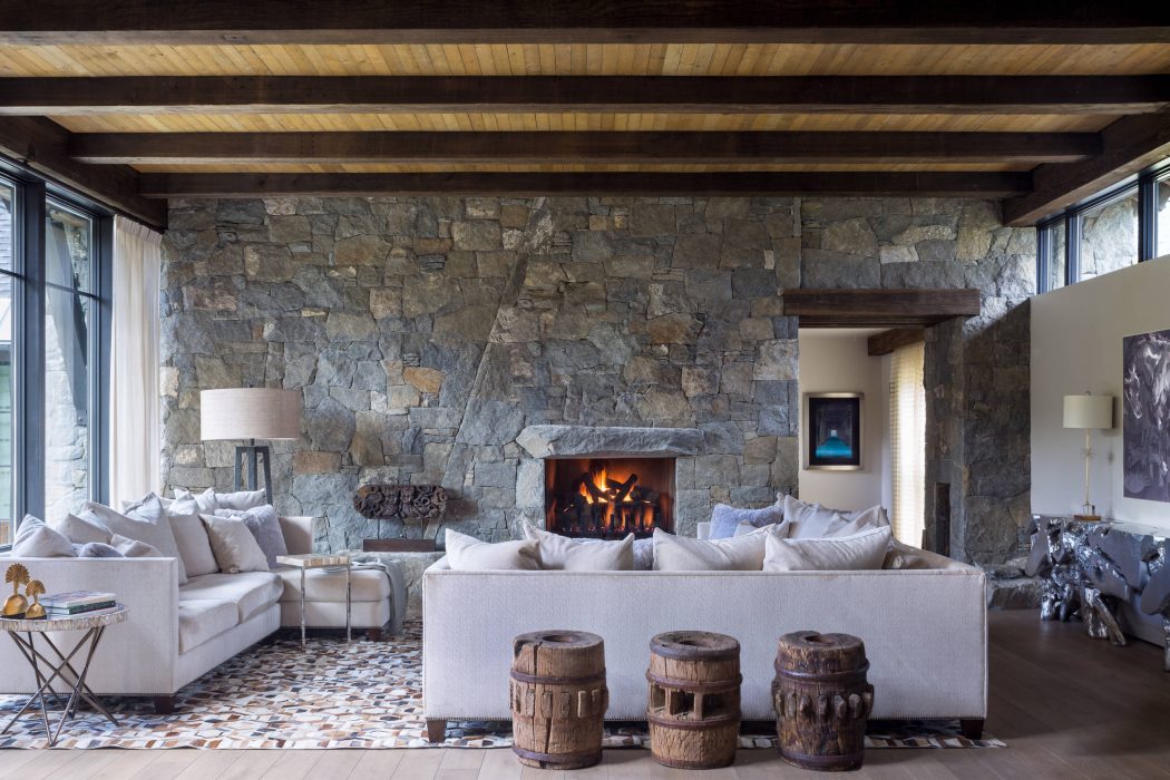 Cozy, rustic living room with exposed stone walls, wooden beams, and a roaring fireplace.