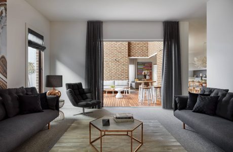 Spacious contemporary living room with plush sofas, hexagonal coffee table, and brick accent wall.