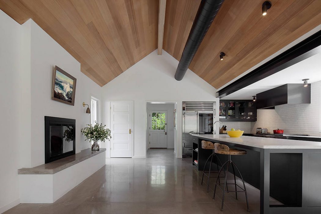 Open-concept kitchen with modern cabinetry, wooden ceiling beams, and a minimalist fireplace.