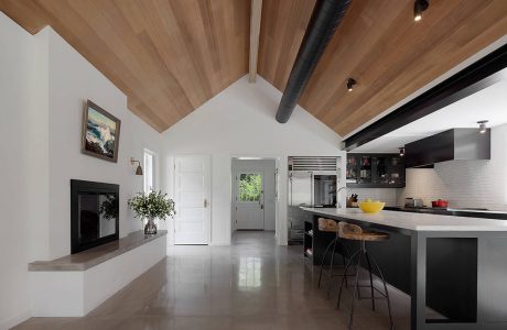 Open-concept kitchen with modern cabinetry, wooden ceiling beams, and a minimalist fireplace.