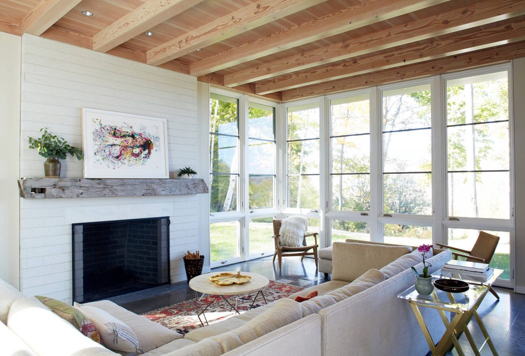 Cozy living room with wood-beamed ceiling, fireplace, and large windows overlooking nature.