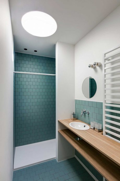Bright, minimalist bathroom with teal subway tiles, wooden vanity, and circular mirror.