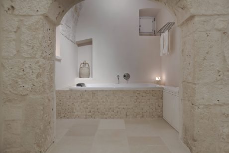 Rustic bathroom design with stone walls, tiled bathtub, and minimal modern fixtures.
