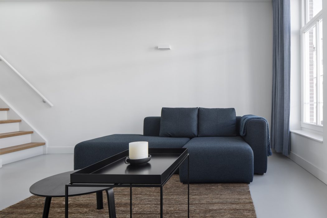 A modern, minimalist living space with a charcoal gray sofa, a low black coffee table, and a simple white candle.