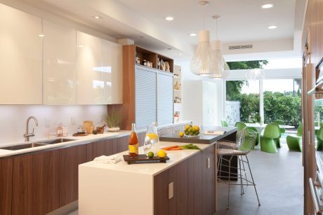 A modern kitchen with sleek wood and white cabinets, a large counter, and pendant lights.