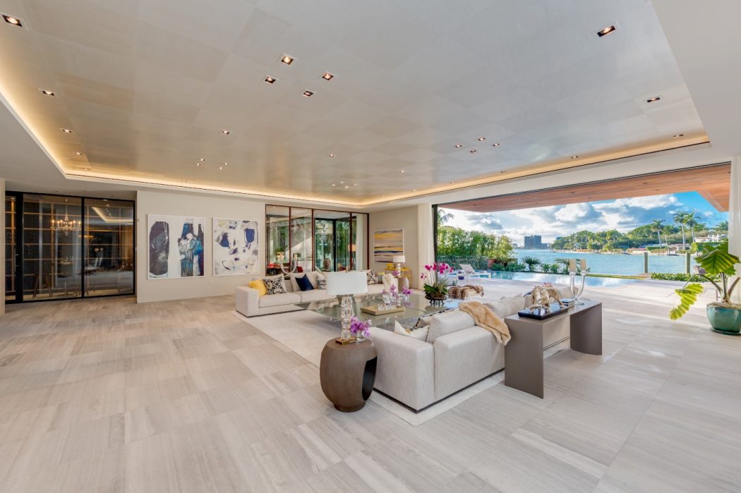 Spacious modern living room with floor-to-ceiling windows, recessed lighting, and waterfront view.