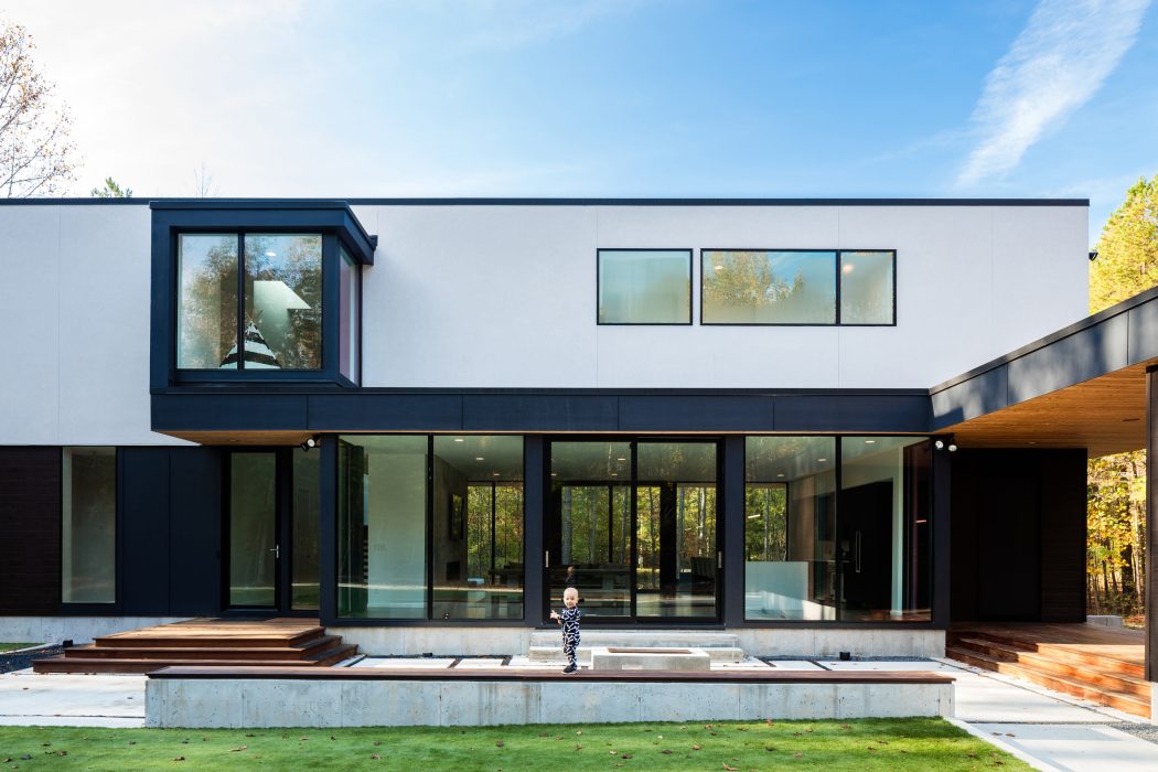 Modern, minimalist home design with extensive glass walls, wooden decks, and a person in the foreground.
