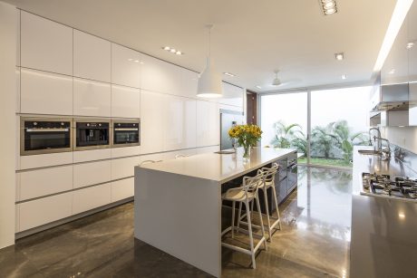Sleek, modern kitchen with white cabinets, island, and large windows overlooking greenery.