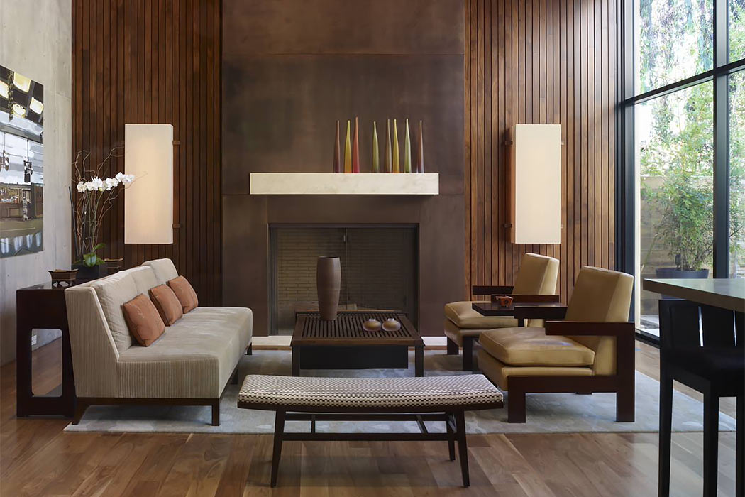 Warm, modern living room with wood-paneled ceiling, concrete fireplace, and large windows.