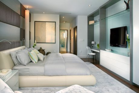 Chic contemporary bedroom with sleek furnishings, warm lighting, and glass wall accents.