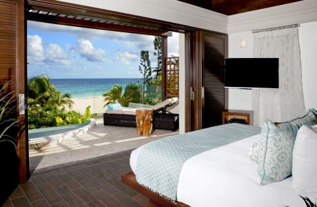 A luxurious bedroom with a view of the tropical beach and ocean through sliding glass doors.