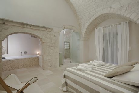 Rustic stone walls, arched entryways, and minimalist furnishings create a serene, spa-like retreat.