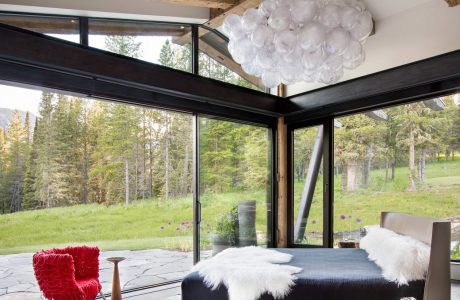 Rustic cabin interior with wood beams, floor-to-ceiling windows, and a modern light fixture.