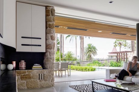 Spacious modern interior with stone wall, wooden beams, and expansive windows overlooking lush greenery.