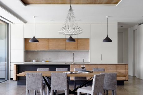 A modern kitchen with wood cabinetry, pendant lighting, and a dining table with chairs.