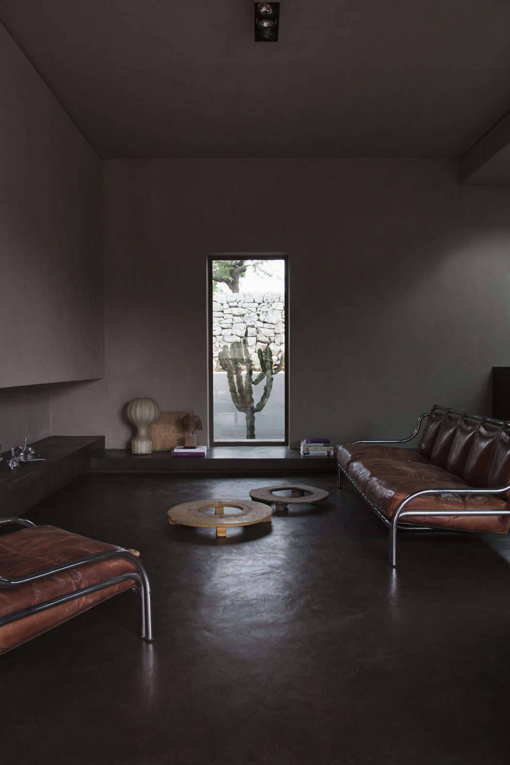 Minimalist, earthy-toned living room with leather couches, artwork, and a large window.