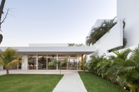 Modern, minimalist architecture with sprawling glass facade, lush tropical landscaping.