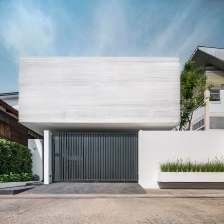 A modern, minimalist building with a clean white facade, contrasting with the dark metal gate.