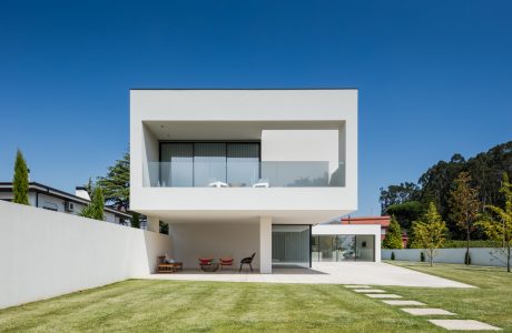 Modern, minimalist house with clean lines, large windows, and a covered patio on a lush, grassy lawn.