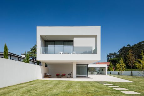 Modern, minimalist house with clean lines, large windows, and a covered patio on a lush, grassy lawn.