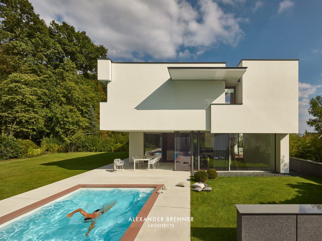 A modern, minimalist house with a swimming pool and lush green surroundings.