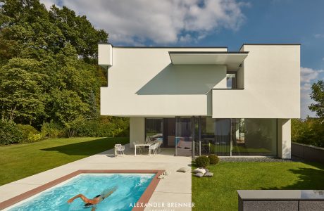 A modern, minimalist house with a swimming pool and lush green surroundings.