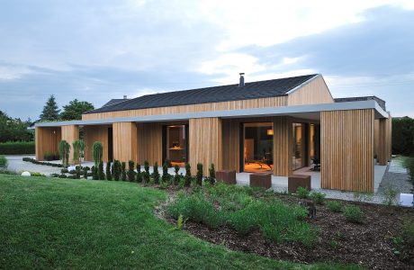 Modern single-story house with wood siding, large windows, and landscaped grounds.