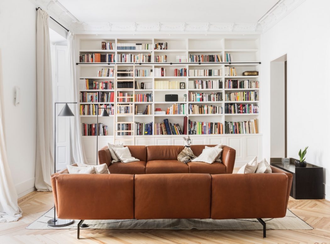 Spacious living room with floor-to-ceiling bookshelves, cozy leather sofa, and hardwood floors.