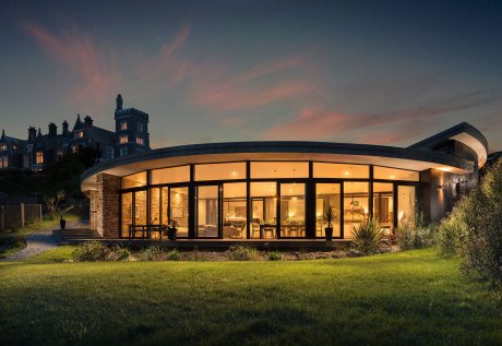 Elegant contemporary glass and stone structure against a historic backdrop at sunset.