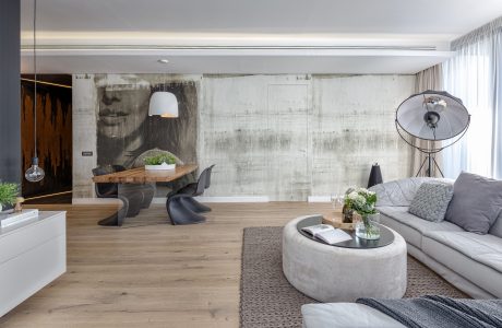Minimalist living room with concrete walls, wood furniture, and modern lighting fixtures.