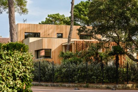 A modern, wooden-clad building nestled among lush greenery and pine trees.