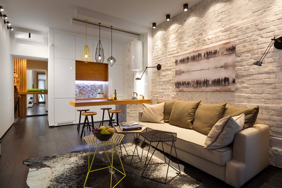 Open-concept living space with exposed brick wall, modern lighting, and minimalist furnishings.