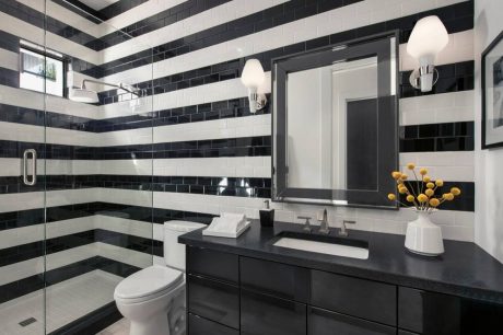 A modern bathroom with striking black and white striped tile walls, a vanity, and lighting fixtures.