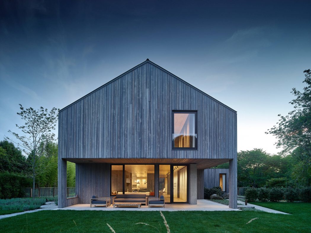 Sleek, minimalist wooden house with large windows, surrounded by lush greenery.