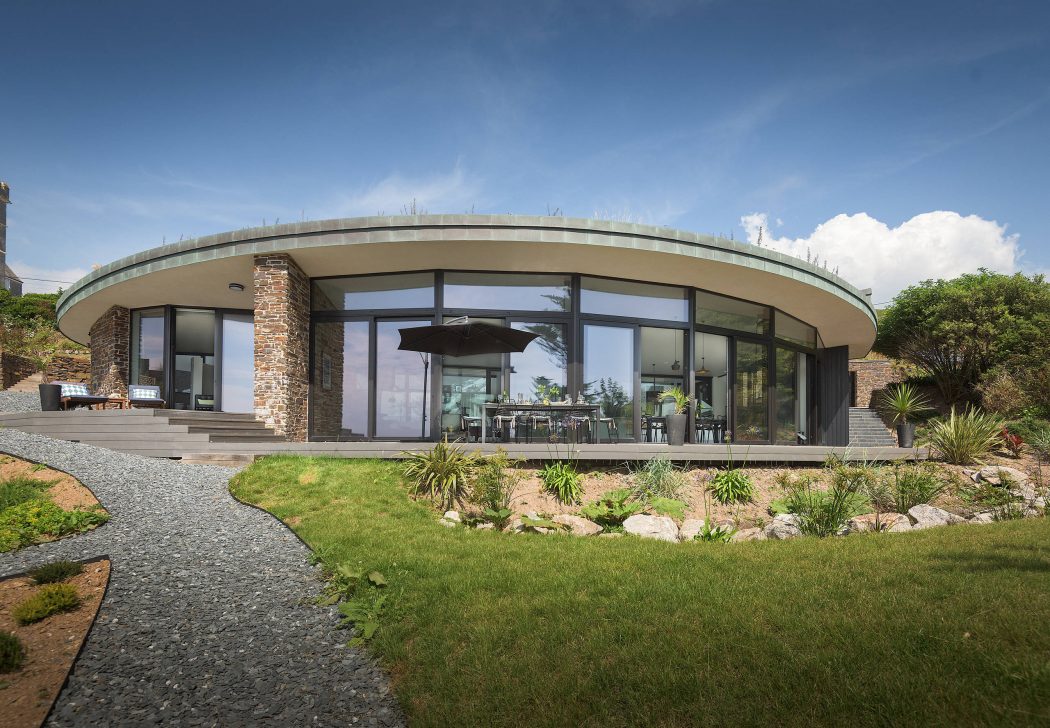 A modern, curved glass and stone building with an expansive patio and landscaping.