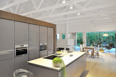 Modern kitchen with sleek gray cabinets, integrated appliances, and a large central island overlooking an open living area with floor-to-ceiling windows.